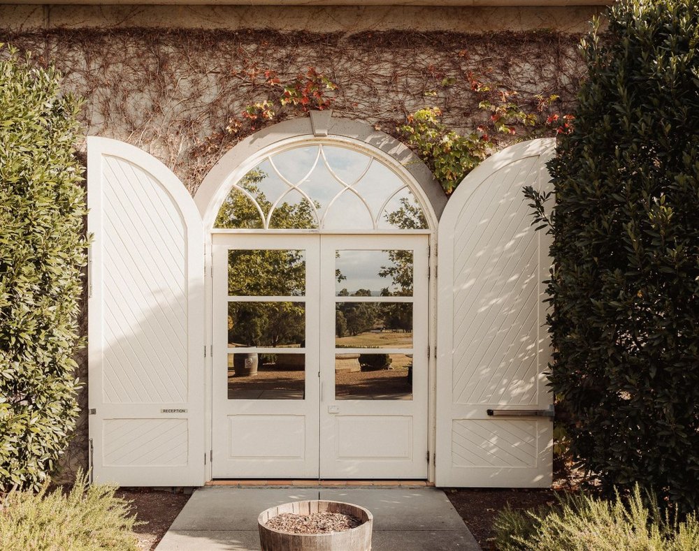 Arched white doors standing open in an ivy-covered stone wall at a wedding venue.