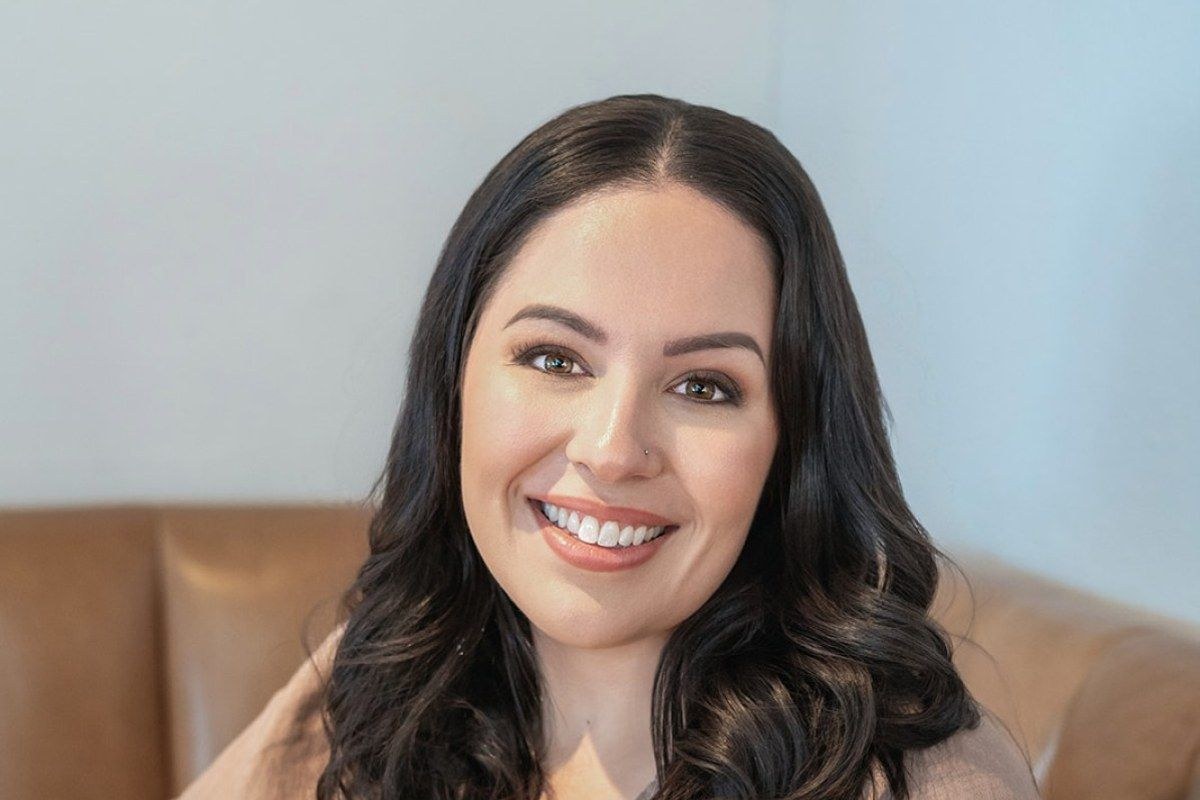 Sheereen, a Melbourne marriage celebrant and MC, smiling on a tan leather couch.