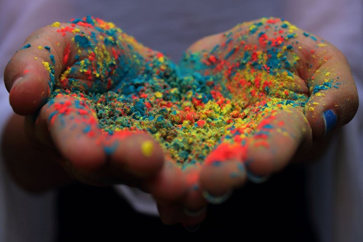 Cupped hands holding brightly coloured Holi festival powder in red, blue, yellow and green.