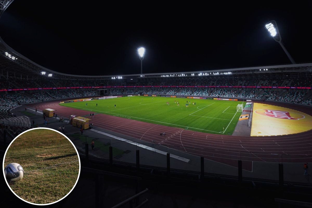 A floodlit football stadium at night, players on a green pitch under bright spotlights.