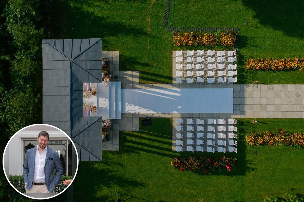 An aerial view of a prepared outdoor wedding venue, with rows of white chairs either side of an aisle runner leading to a pavilion.