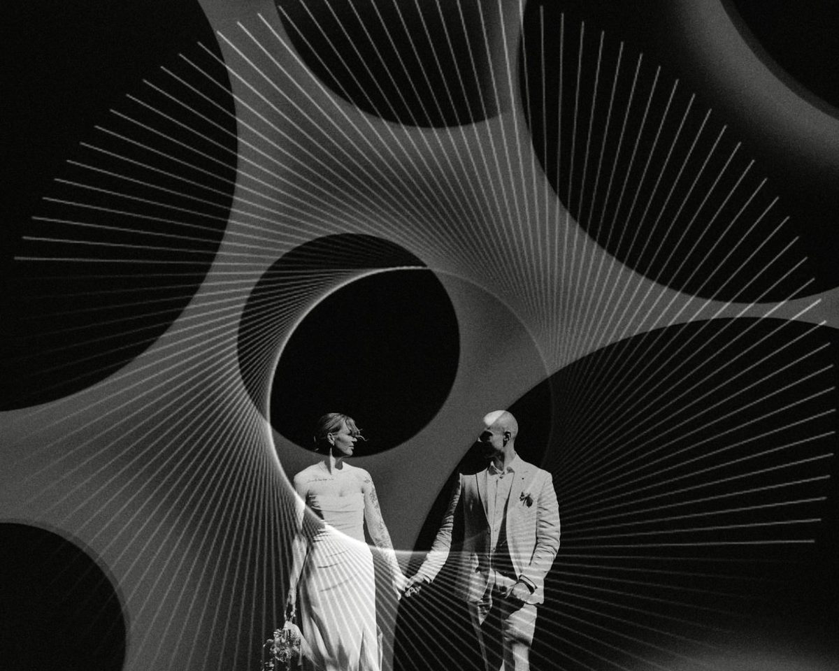 A black and white photograph of a couple standing at the centre of a large radiating spiral structure.