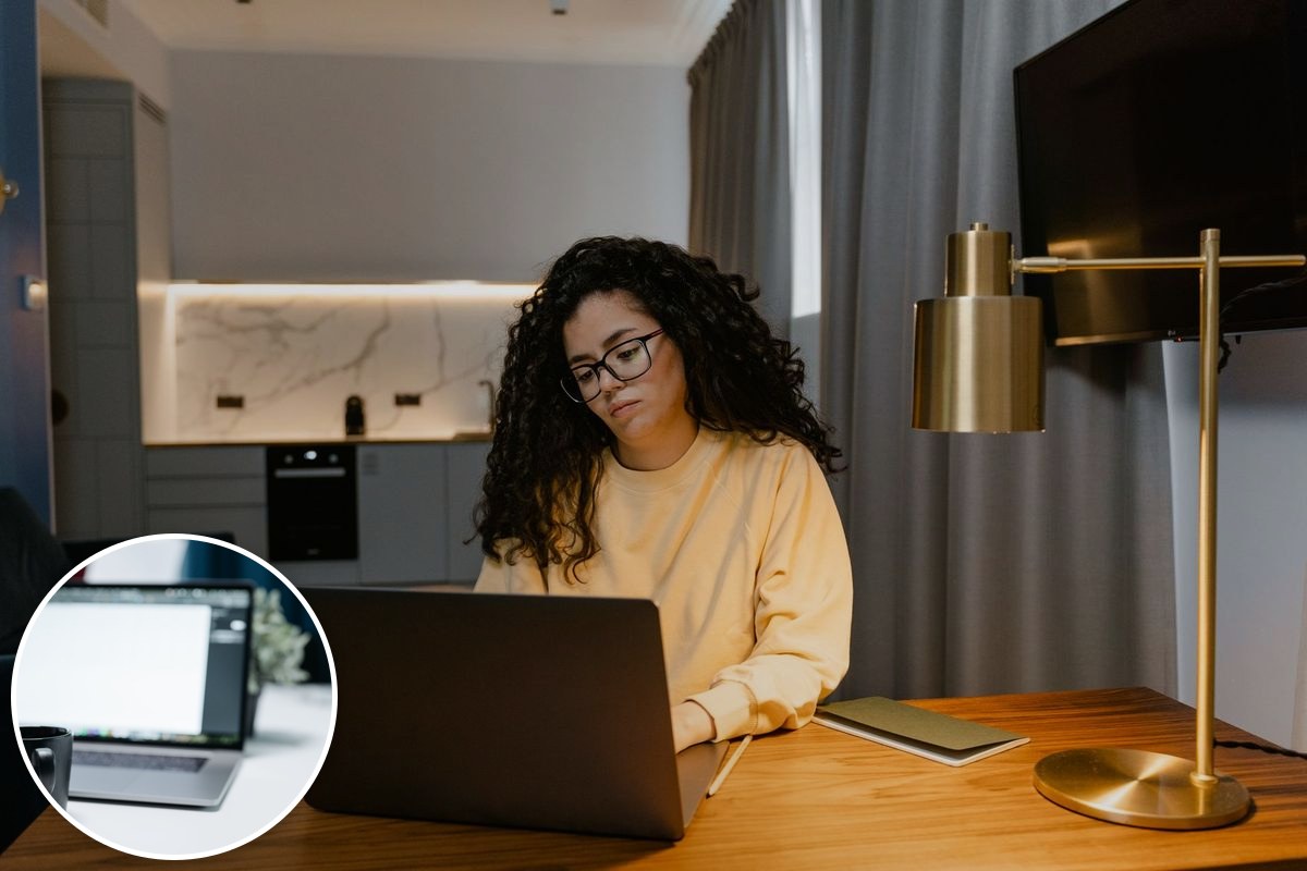 A woman in a yellow sweatshirt working on a laptop at a desk in a bright, modern home interior.