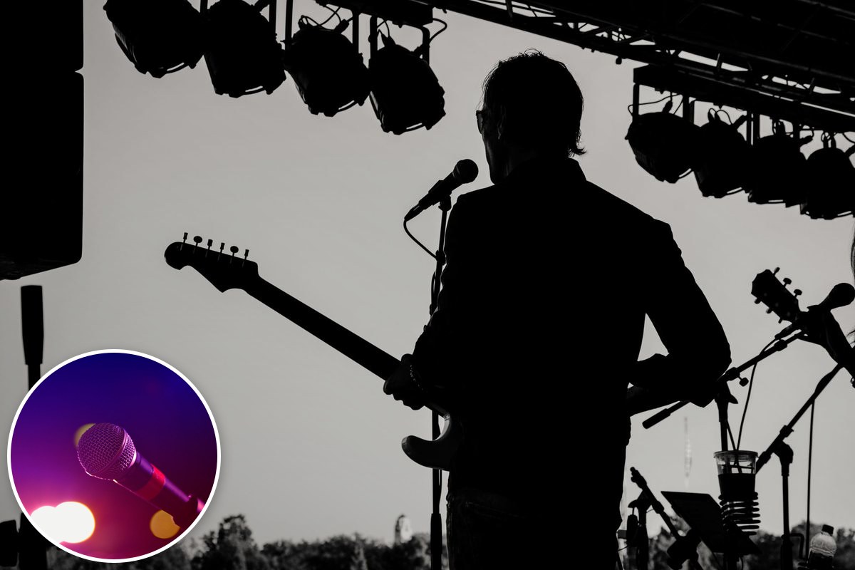 Silhouette of a guitarist singing at a microphone on an outdoor stage under lighting rigs.