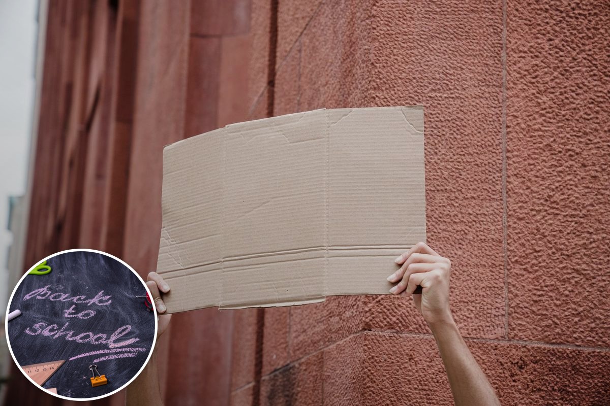 A pair of hands holds a blank cardboard placard aloft against a red brick wall.