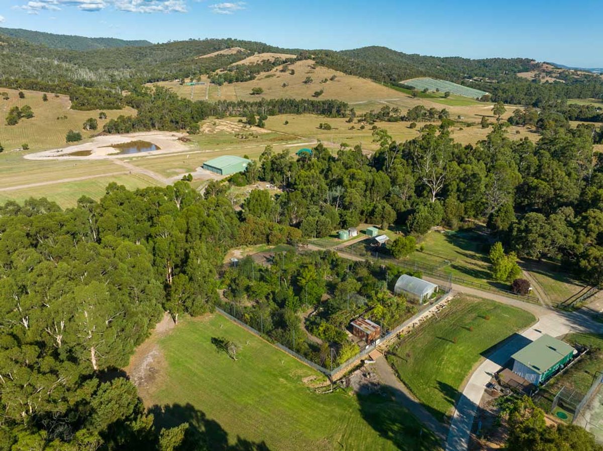 Aerial view of Yarra Valley Estate's bushland property, with its airstrip, sheds and the fenced Edible Forest among the trees.