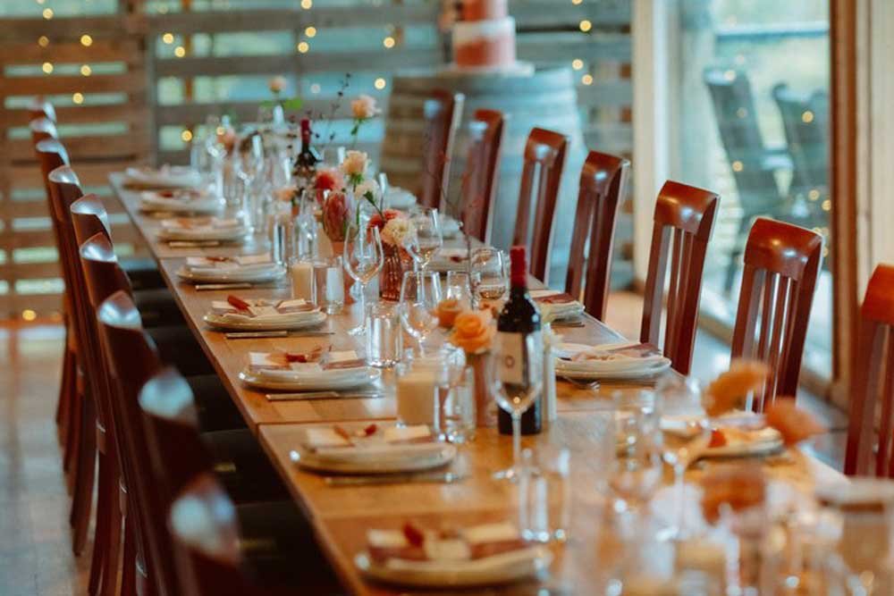 A long wedding table dressed with flowers, candles and wine under fairy lights in a timber-lined function room at Yarra Valley Estate.