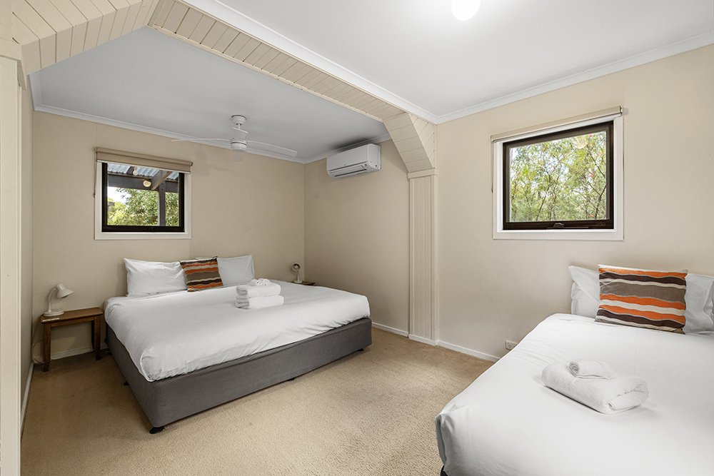 A bright ensuite guest room at Yarra Valley Estate with a queen bed, single bed and bushland views through the windows.